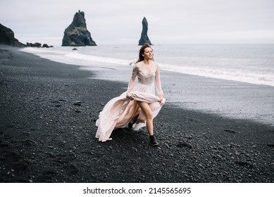 Beautiful young girl in wedding dress and black boots run on Black Sand beach in Vic, Iceland with high rock islands in background - Powered by Shutterstock