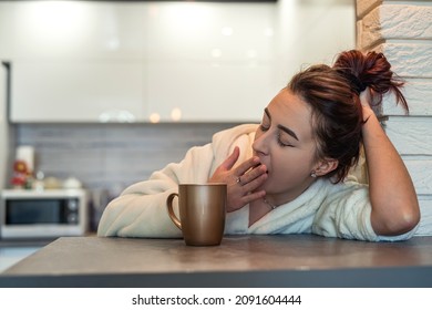 beautiful young girl in a white coat and sneakers sleepy in the morning brews coffee in her own kitchen. Sleepy woman concept