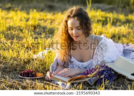 Beautiful young girl in a white dress, straw hat, picnic basket reading a book on a meadow. Summertime, golden hour, sunset. Concept of work life balance SSTKHome
