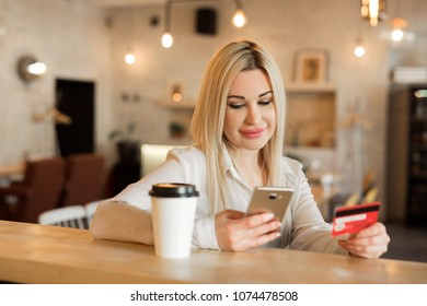 beautiful young girl in white shirt with phone and plastic card in hands