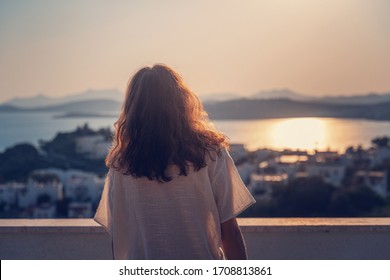 Beautiful  young girl woman on a city at sunset and on the sea and nature from the roof or a balcony. Standing with his back to the camera, no face.