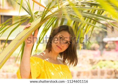 Beautiful young girl in yellow dress posing under palm leaves
