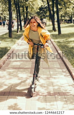 Beautiful young girl in a yellow raincoat riding an electric scooter, hoverboard, in orange sunglasses with long hair, street-style, city, smiles and pleasure, for fan, hipster, driver, emotional