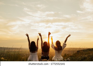 Beautiful young girls girlfriends on a picnic on a summer day. The concept of leisure, privacy, communication, vacation. Group of women enjoying picnic in the countryside with the perfect sunset.