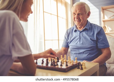 Beautiful young girl-volunteer and handsome old man are playing chess and smiling