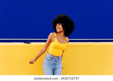 Beautiful young happy african woman with afro curly hairstyle strolling in the city - Cheerful black student portrait on colorful wall background - Powered by Shutterstock