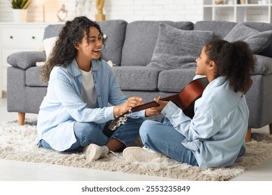 Beautiful young happy African-American mother teaching her daughter playing guitar at home - Powered by Shutterstock