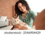 Beautiful young happy African-American woman with her cute Maine Coon cat taking selfie at home