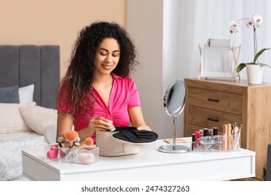 Beautiful young happy African-American woman with storage box doing makeup at home