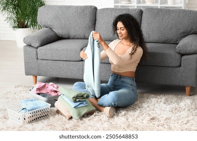 Beautiful young happy African-American woman folding clean clothes at home - Powered by Shutterstock