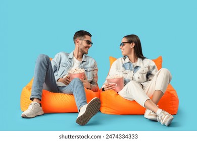 Beautiful young happy couple with buckets of popcorn watching TV on beanbag chairs against blue background - Powered by Shutterstock