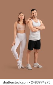 Beautiful young happy couple in sportswear doing exercises on brown background