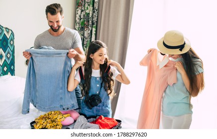 Beautiful Young Happy And Excited Family In A Luxury Hotel Room While Unpacking Stuff And Clothes And Having Fun Together. Vacation Or Trip In Summer