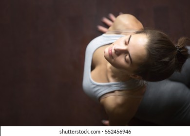 Beautiful young happy model girl working out in home interior, doing yoga exercise on wooden floor, stretching in upward facing dog or cobra pose. High angle view. Copy space