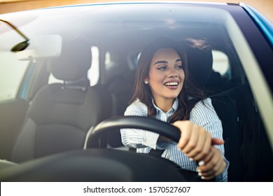 Beautiful Young Happy Smiling Woman Driving Her New Car At Sunset. Young Woman Driving A Car In The City. Portrait Of A Beautiful Woman In A Car, Looking Out Of The Window And Smiling. 