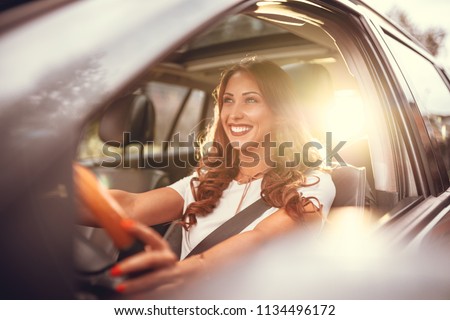 Beautiful young happy smiling woman driving her new car at sunset. 