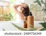 Beautiful young happy woman with bottles of shampoo washing hair in bathroom at home