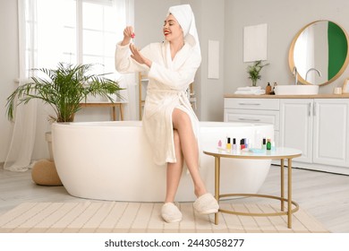 Beautiful young happy woman with bottles of nail polish doing manicure in bathroom - Powered by Shutterstock