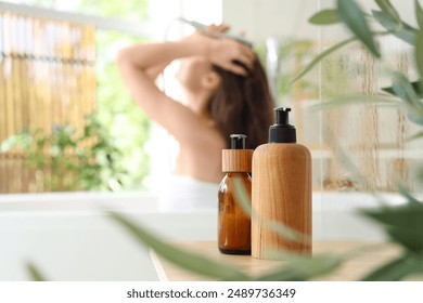 Beautiful young happy woman with bottles of shampoo washing hair in bathroom at home