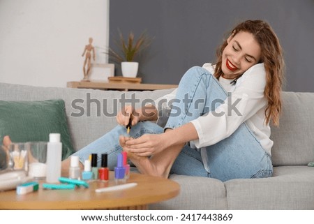 Beautiful young happy woman doing pedicure and talking by mobile phone in living room