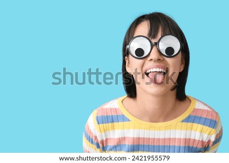Beautiful young happy woman in funny disguise showing tongue on blue background. April Fools Day celebration