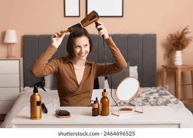 Beautiful young happy woman with hairdryer, brush and hair care products at home - Powered by Shutterstock