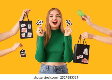 Beautiful young happy woman with percent signs and hands holding shopping bags, credit card on yellow background. Black Friday sale - Powered by Shutterstock