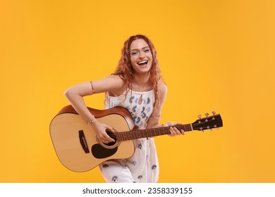 Beautiful young hippie woman playing guitar on orange background - Powered by Shutterstock