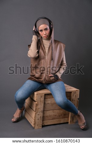 Beautiful young hipster girl wearing  hijab and listening to music with wireless headphones isolated over grey background. Technology in a modern lifestyle concept.