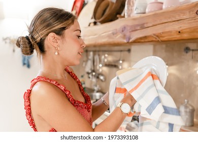 Beautiful Young Hispanic Wife With Typical Cute Dress Washing And Drying Dishes After Home Party With Friends. Real Woman Busy Helping With Housework. Concept Of Women's Work Never Stops Even At Home