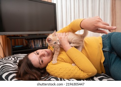 Beautiful Young Hispanic Woman Dressed In A Yellow Jacket, Lying On Her Bed Hugging And Playing With Her Little Light Brown Cat