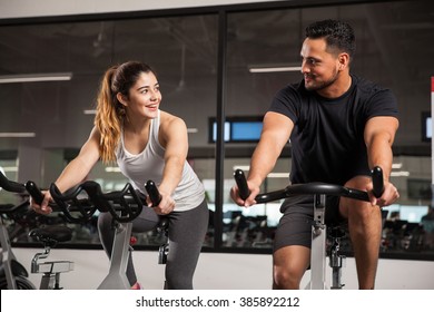 Beautiful Young Hispanic Woman Flirting And Talking To A Guy While They Both Do Some Spinning At A Gym. Focus On Woman