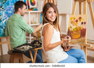 Beautiful young Hispanic woman and a handsome man attending a painting workshop together and having fun
