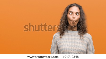 Beautiful young hispanic woman wearing stripes sweater making fish face with lips, crazy and comical gesture. Funny expression.