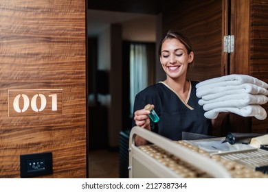 Beautiful young hotel chambermaid in uniform bringing clean towels and other supplies to hotel room.