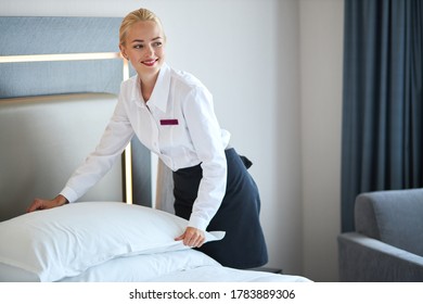 Beautiful Young Hotel Maid Setting Up White Pillow On Bed Sheet In Hotel Room, Smile, Enjoy