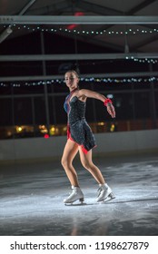 A beautiful young ice skater lifts her arms up in the air during her performance. 