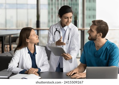 Beautiful young Indian doctor woman holding tablet, talking with colleagues, discussing diagnosis, giving consultation of expert. Multiethnic practitioners using gadgets for work discussion - Powered by Shutterstock