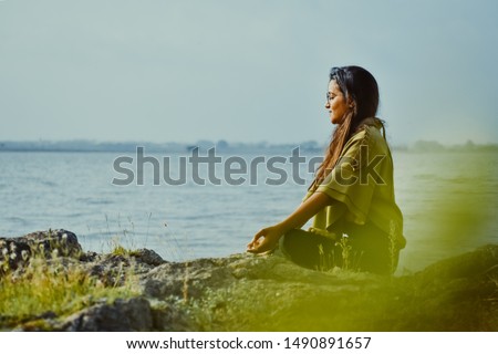 Beautiful young Indian girl practicing yoga on the lake shore at Nyari dam, Rajkot, India.