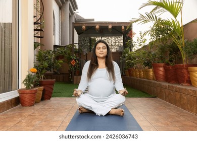 Beautiful young indian pregnant woman doing yoga lotus position at home. Health care concept. - Powered by Shutterstock