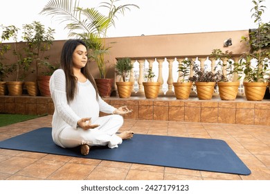 Beautiful young indian pregnant woman doing yoga lotus position at home. Health care concept. - Powered by Shutterstock