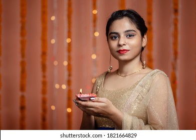 Beautiful Young Indian woman holding burning Diya and looking at camera. Diwali or deepawali celebration with light bokeh in background. - Shutterstock ID 1821664829