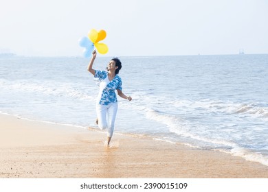 Beautiful young indian woman running with multicolor balloon in hands at the beach. Young girl having fun, holidays and vacation. - Powered by Shutterstock