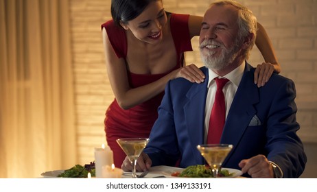 Beautiful Young Lady Massaging Shoulders Of Old Rich Man, Flirting On Date