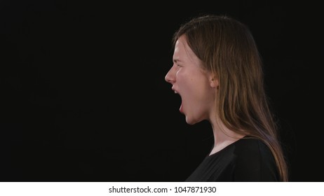 A beautiful young lady shouting against a black background. Close-up shot