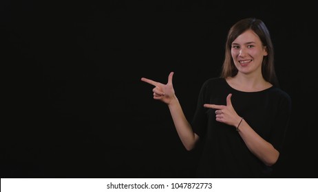 A beautiful young lady smiling and standing and pointing with her finger against a black background. Medium Shot