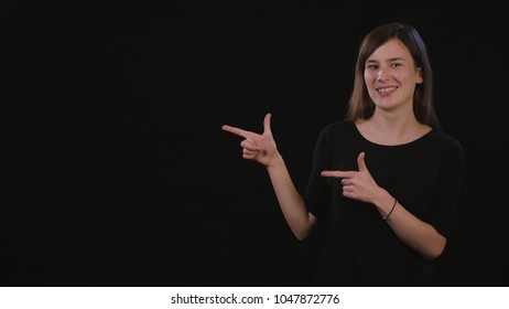 A beautiful young lady smiling and standing and pointing with her finger against a black background. Medium Shot