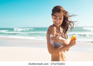 Beautiful young latin woman applying suntan lotion at sea with copy space. Tanned girl in bikini applying sunscreen on shoulder at tropical beach. Woman protecting skin with sunblock cream from UV. - Powered by Shutterstock