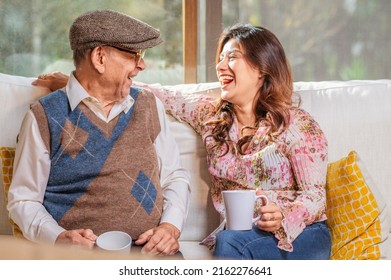 A beautiful young Latin woman enjoys a cup of coffee with her older father on the sofa in their living room. 