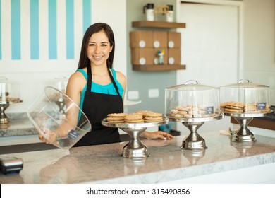 Beautiful young Latin woman showing some of the products she sells in her cake shop and smiling